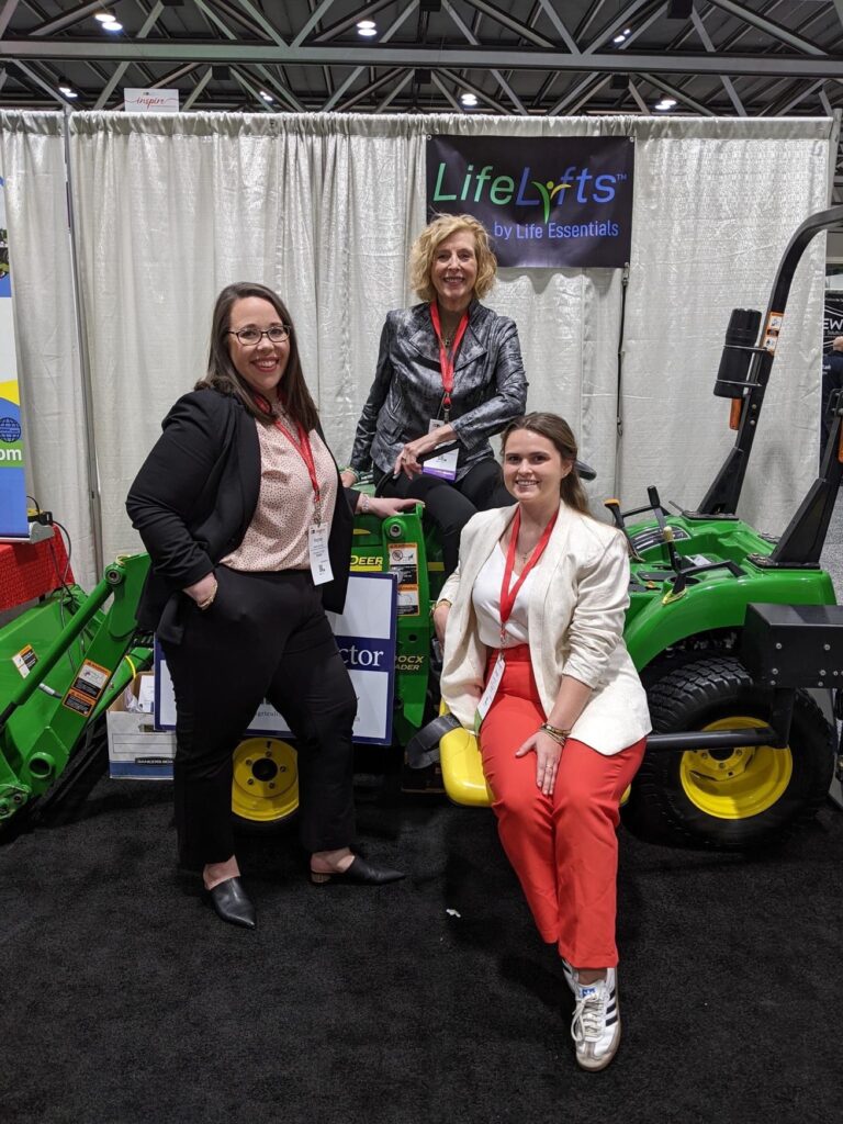 Photo shows Meghan Skidmore, Maggie Mencer, and Mary Smith on a John Deere tractor lift at the AOTA conference